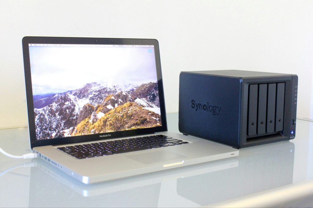A four bay NAS - Network Attached Storage) beside an Apple MacBook Pro