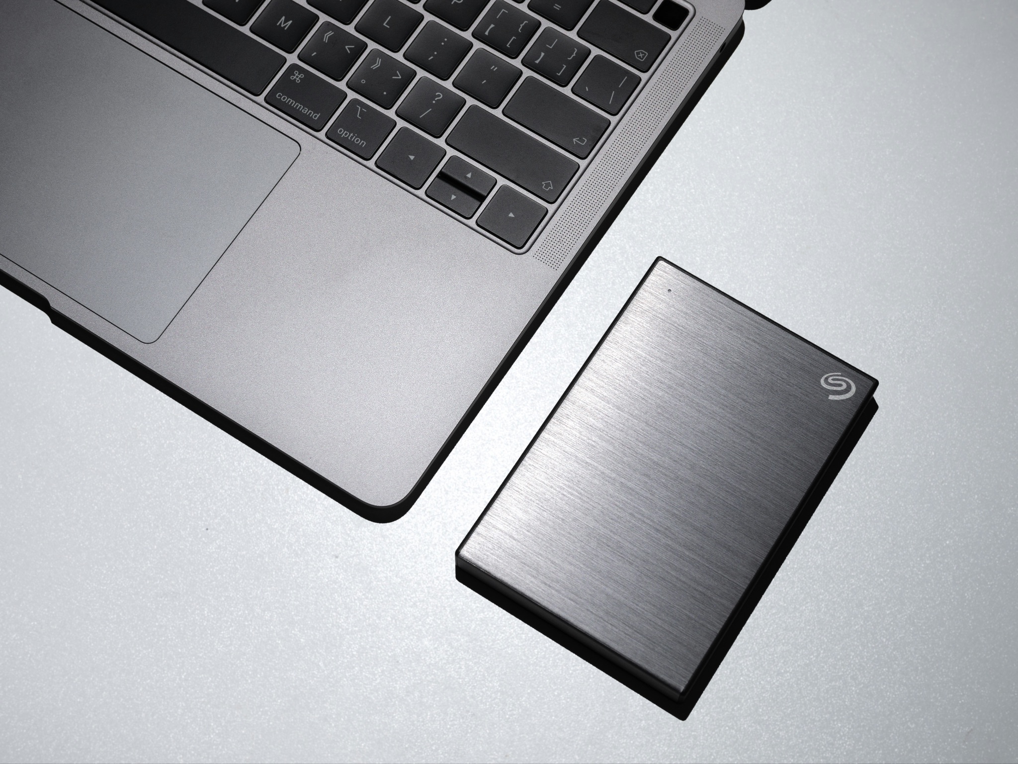 An external hard drive beside an Apple Mac laptop. 